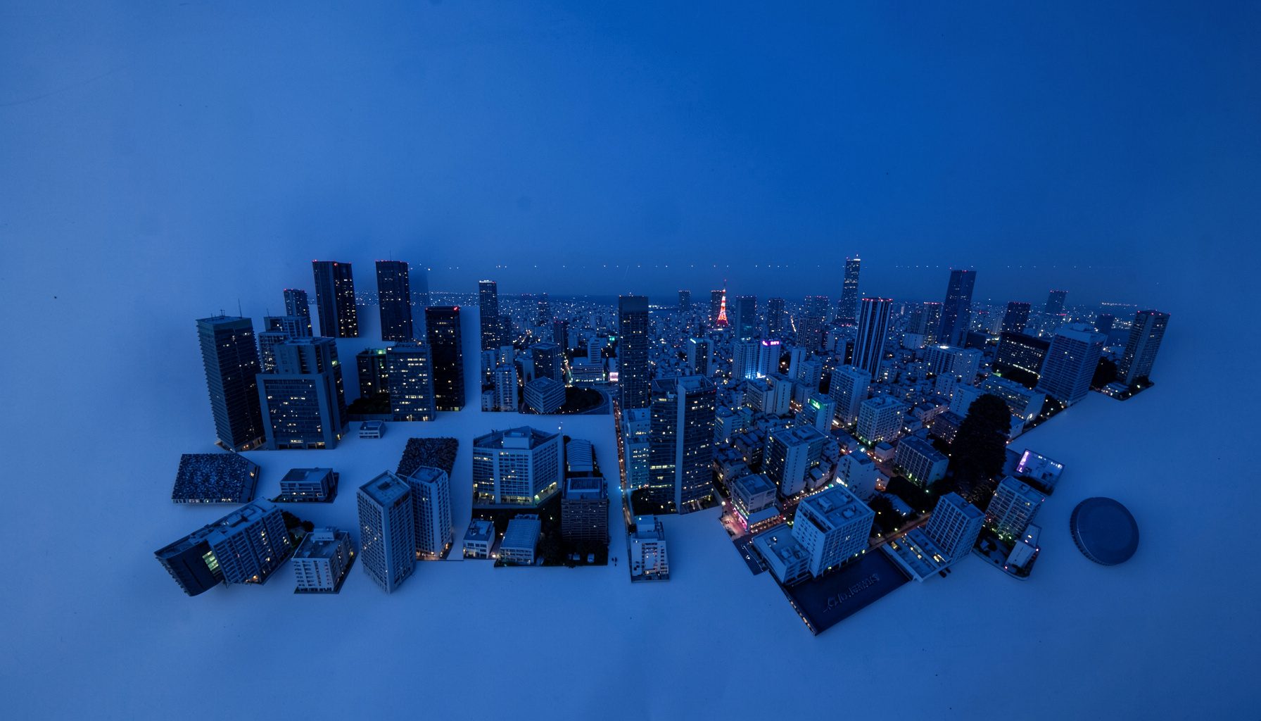 Aerial view of the Tokyo skyline at dusk, deep blue sky with scattered city lights and the silhouette of high-rise towers stretching across the frame